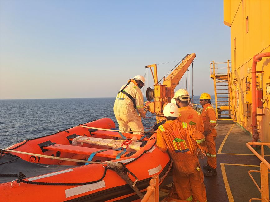 Crew members in protective gear ready a lifeboat during an offshore safety drill on a ship.